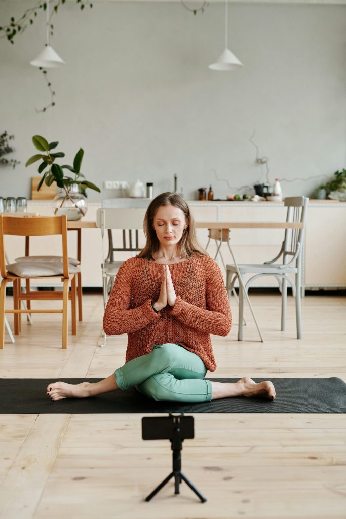 pexels photo 4151130 4151130 Woman practicing yoga on a mat indoors, with smartphone setup for video.